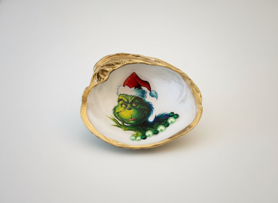Decorative clam shell with a painted Grinch green character wearing a red hat on a brown fabric background